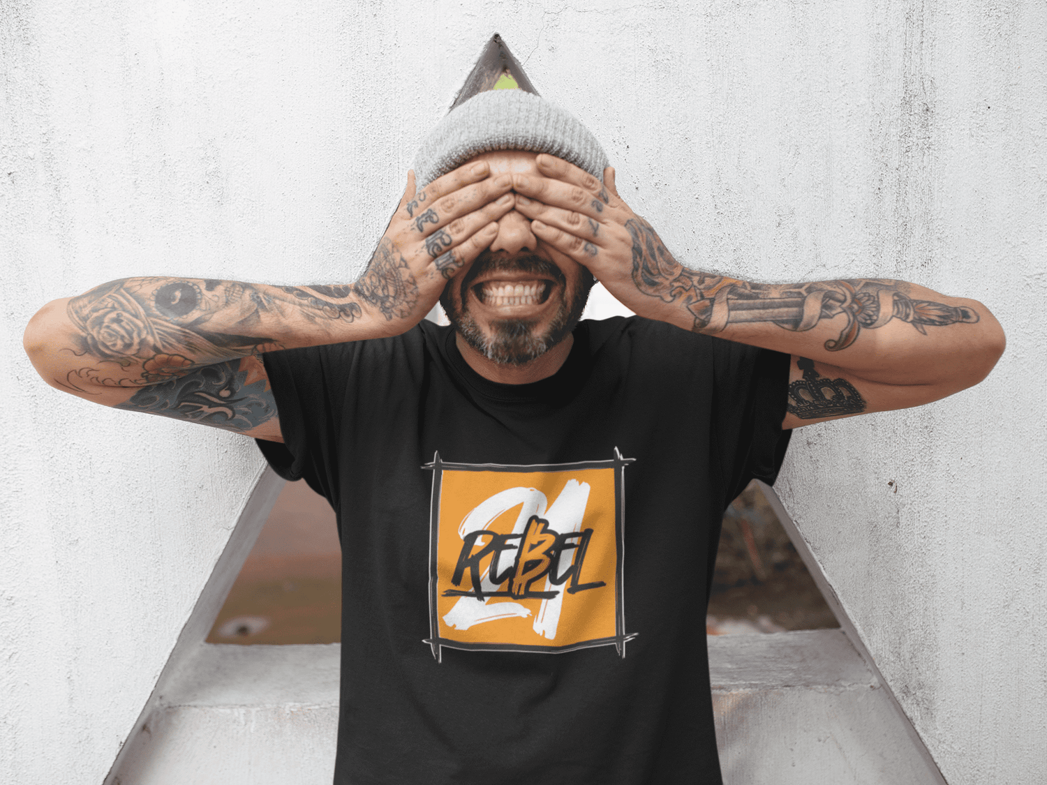 Tattoed man covering his eyes, wearing a black 21 rebel bitcoin shirt.