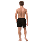 Back view of a man wearing a black bitcoin swim trunks.