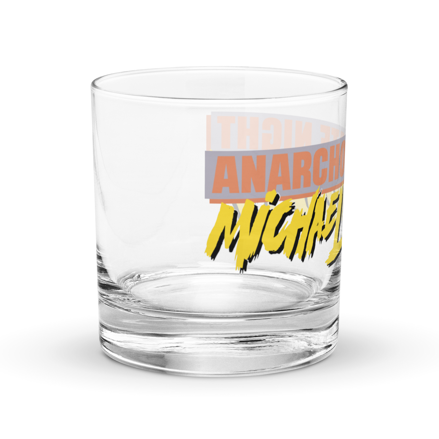 Michael Monday Anarcho Late Night rocks glass, clear 10.5 oz whiskey glass with a band running all the way around: ANARCHO LATE NIGHT in orange on grey above the name Michael Monday in yellow brush script, right side view showing ANARCHO and the start of the name.