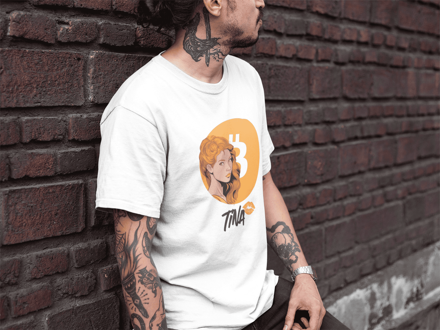 Tattooed middle aged man wearing a white bitcoin t-shirt while leaning against a bricks wall.